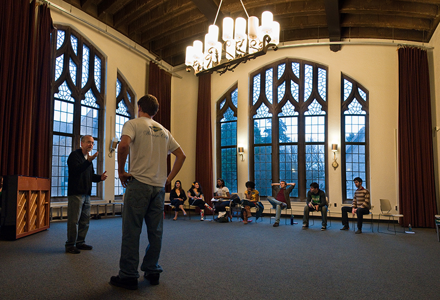 Two people talking to eachother in front of a group of seated observers