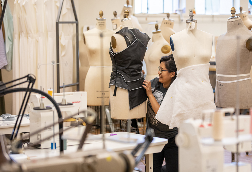 Student pinning/stiching garment together on a dress form