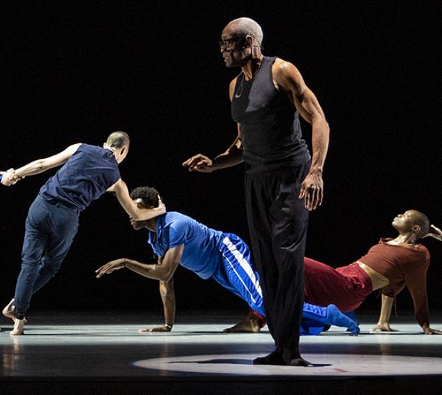 Four performers illuminated on a stage against a dark background