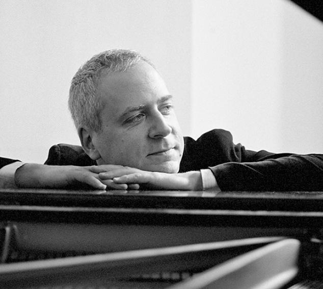 Black and white photo of a man posing on a piano against a light background