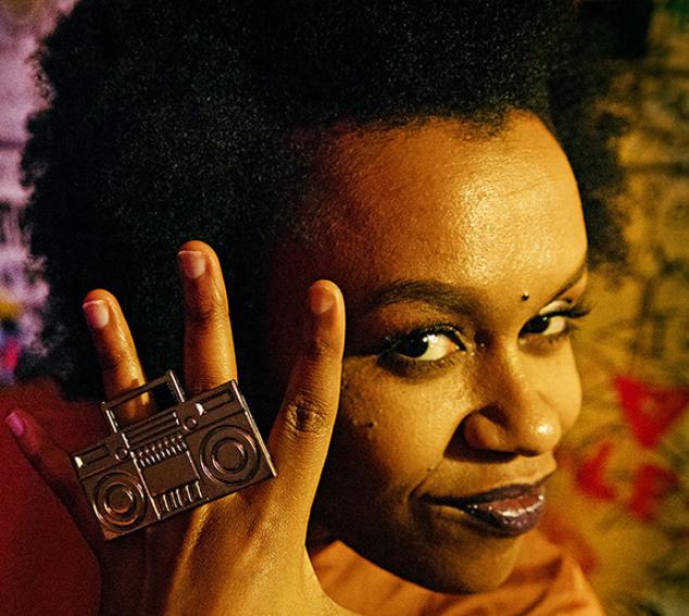 Close up of a woman with a boombox style ring against a pattern background