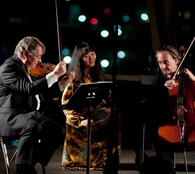 David Finckel, Wu Han, and Philip Setzer playing instruments outdoors at night.