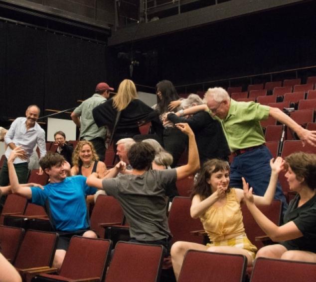 audience members wave their arms and wiggle their bodies as part of graduate symposium lecture.