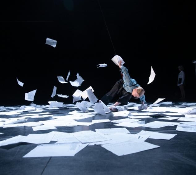 papers flying and a dancer in rope and harness