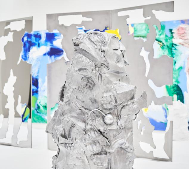 A silvery grey sculpture occupies the forefront of the image, with a background of mirrored sculpture and shades of a blue and green painting.
