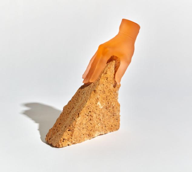 A orange-hued form of a hand grasps a tan rock on a white background