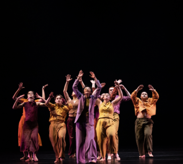 UW Dancers in colorful clothing on stage with their hands up 