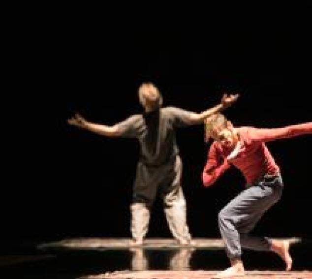 A woman in a twisted, active pose in the foreground and a man with his arms wide and his back to the camera in the background