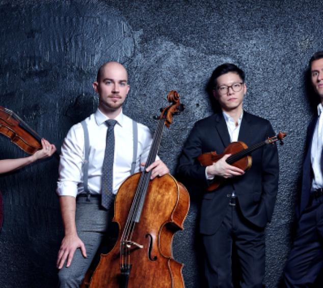 Four musicians pose with their string instruments against a dark background