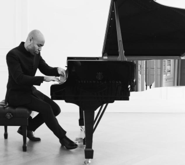 Black and white photo of a man posing on a piano against a light background
