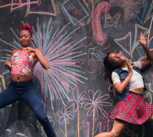 Two female dancers against a colorful chalk wall.