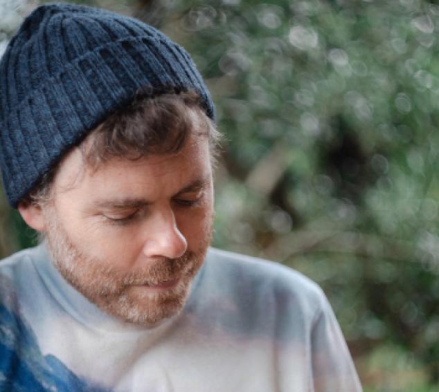 The musician looks away from the camera in front of a natural background