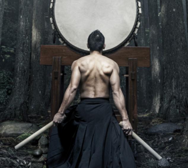 A male performer poses in front of a traditional drum