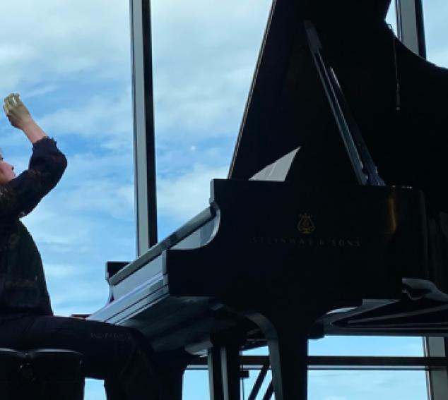 Player sits and plays at piano against blue sky background